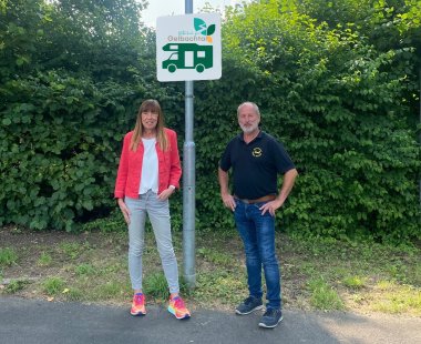 Karin Maas und Reiner Becker stehen vor dem Schild, das den Stellplatz ausweist.