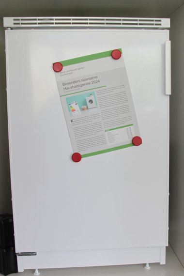 Ein Kühlschrank und die Bröschüre „Besonders sparsame Haushaltsgeräte 2024“.