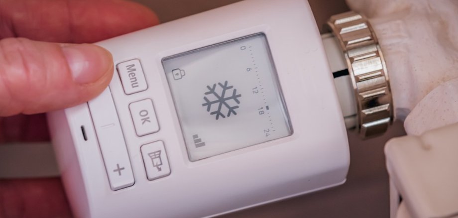 Nahaufnahme einer Hand, die ein digitales Thermostat mit einem Display hält. Auf dem Display wird ein Schneeflockensymbol angezeigt, das auf den Kühl- oder Sparmodus hinweist.